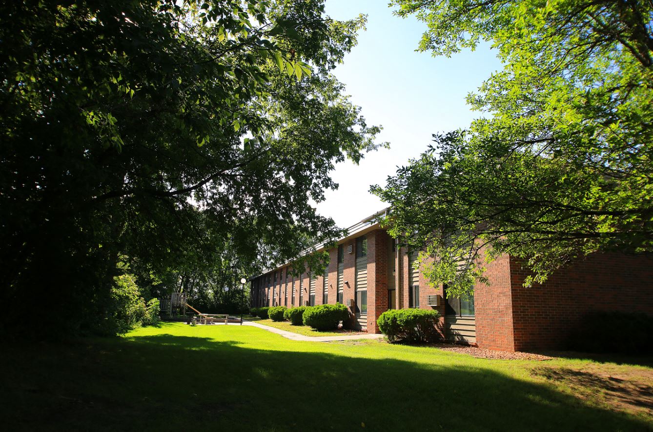 the side of a brick building with grass and trees