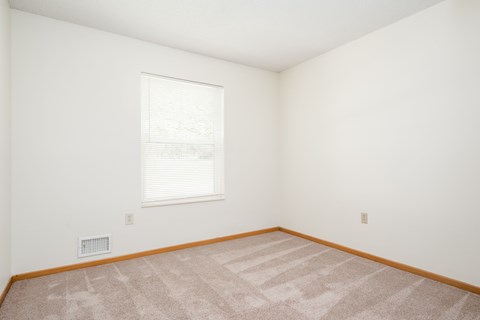 A room with a carpeted floor and a window with blinds.