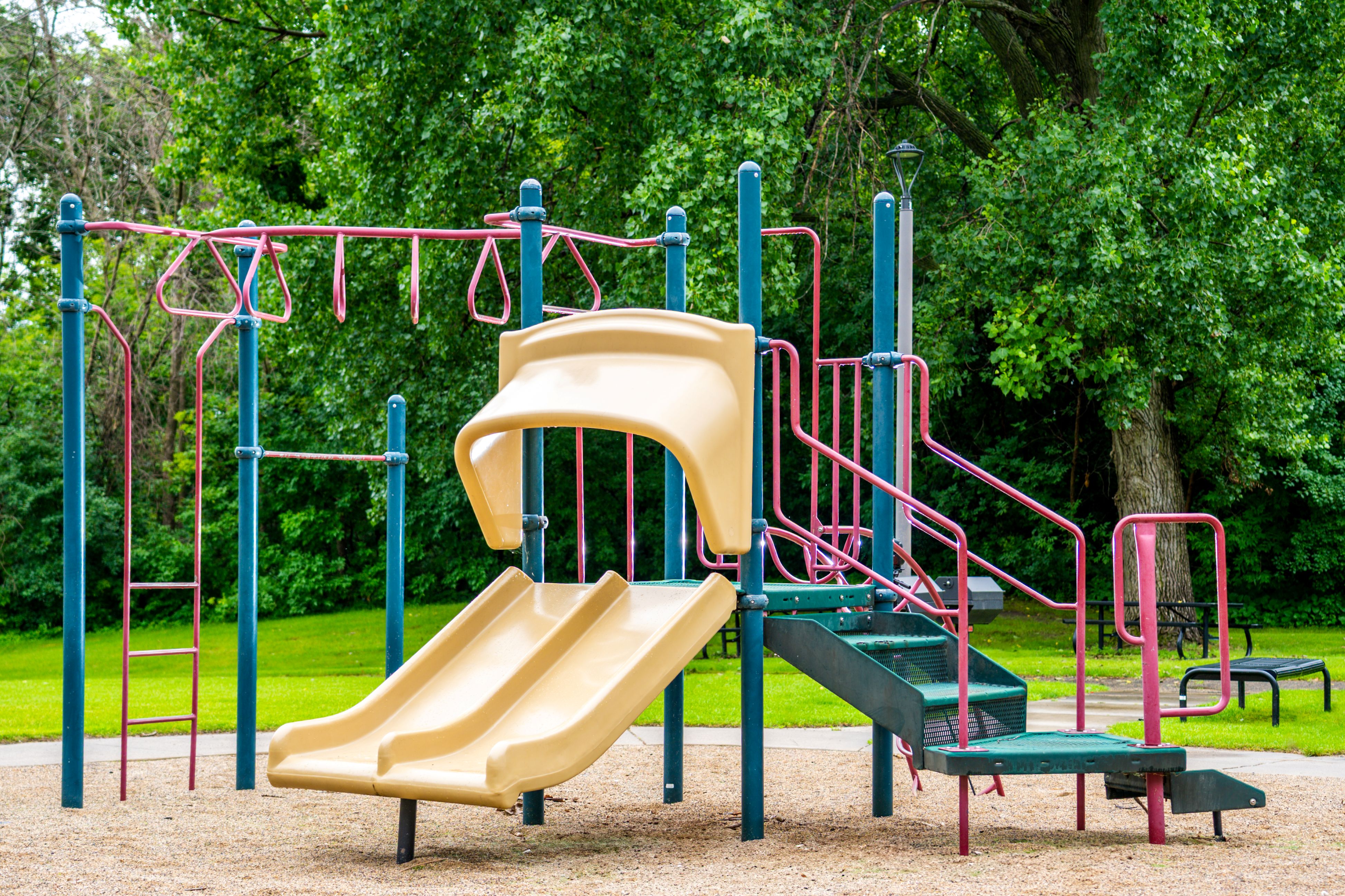A playground with a yellow slide and green and red metal bars.