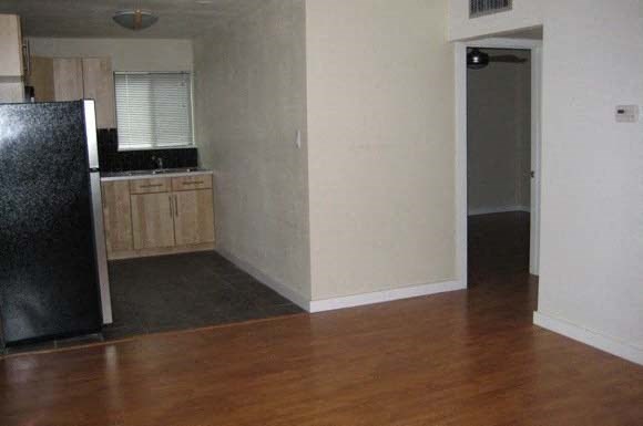 an empty kitchen with wood floors and a black refrigerator