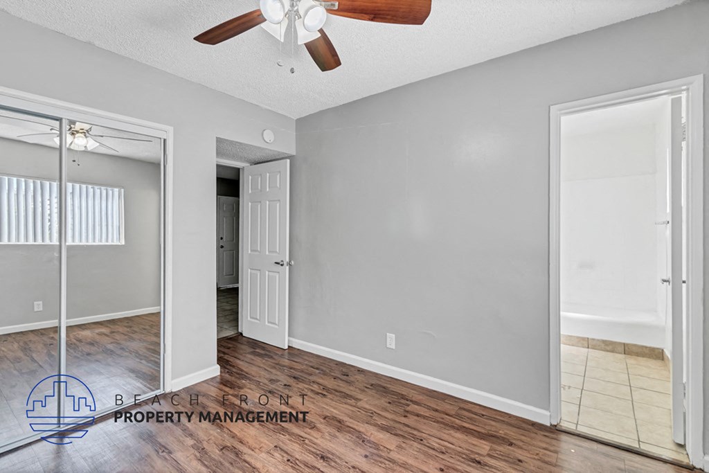 an empty living room with a mirrored closet and a ceiling fan