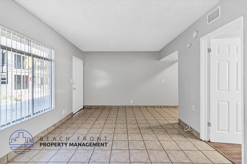 A spacious room with tile flooring and a large window overlooking the street.