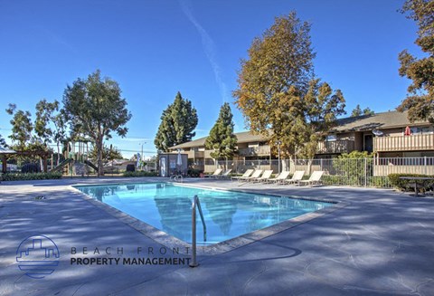 A pool surrounded by trees and chairs with a sign that says Beach Front Property Management.