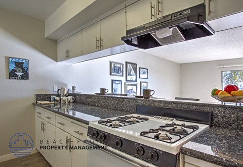 A kitchen with a stove top oven and a bowl of fruit on the counter.