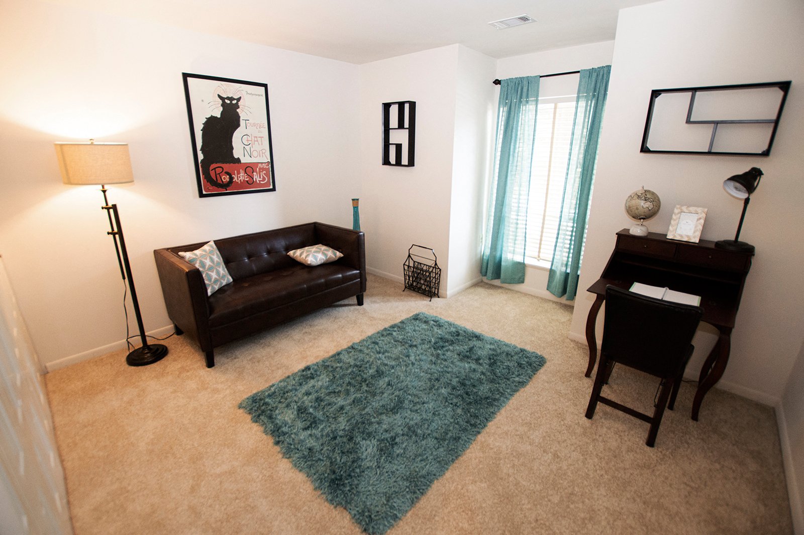 A living room with a black couch and a blue rug.