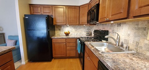 A black refrigerator sits in a kitchen with wooden cabinets.
