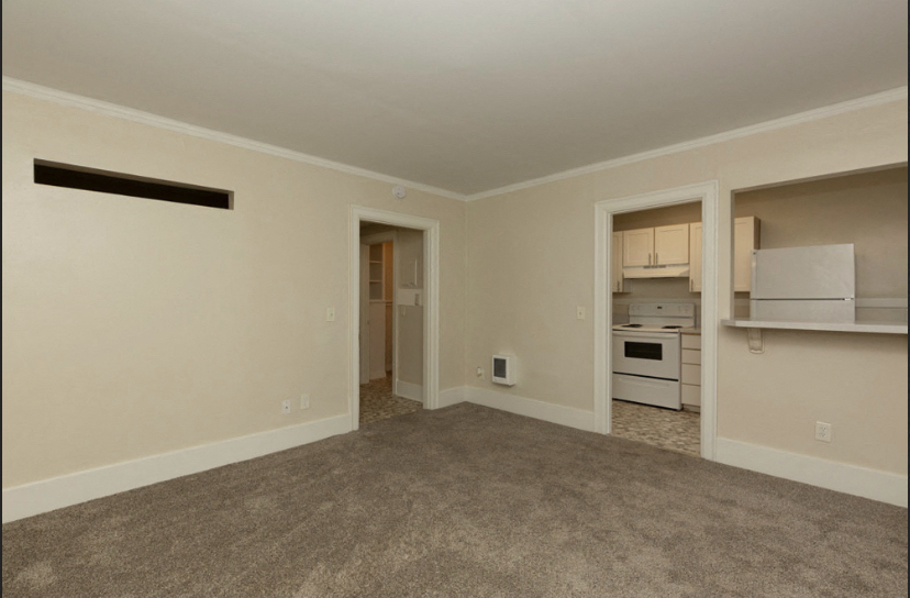an empty living room with a kitchen in the background