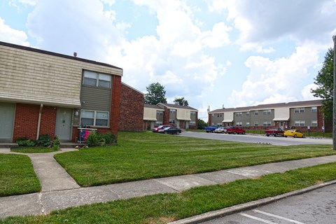 a row of apartment buildings with a lawn and a parking lot