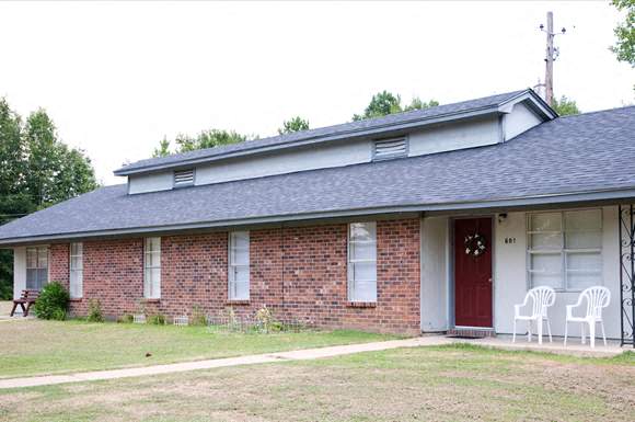 a red brick house with two white chairs on the porch