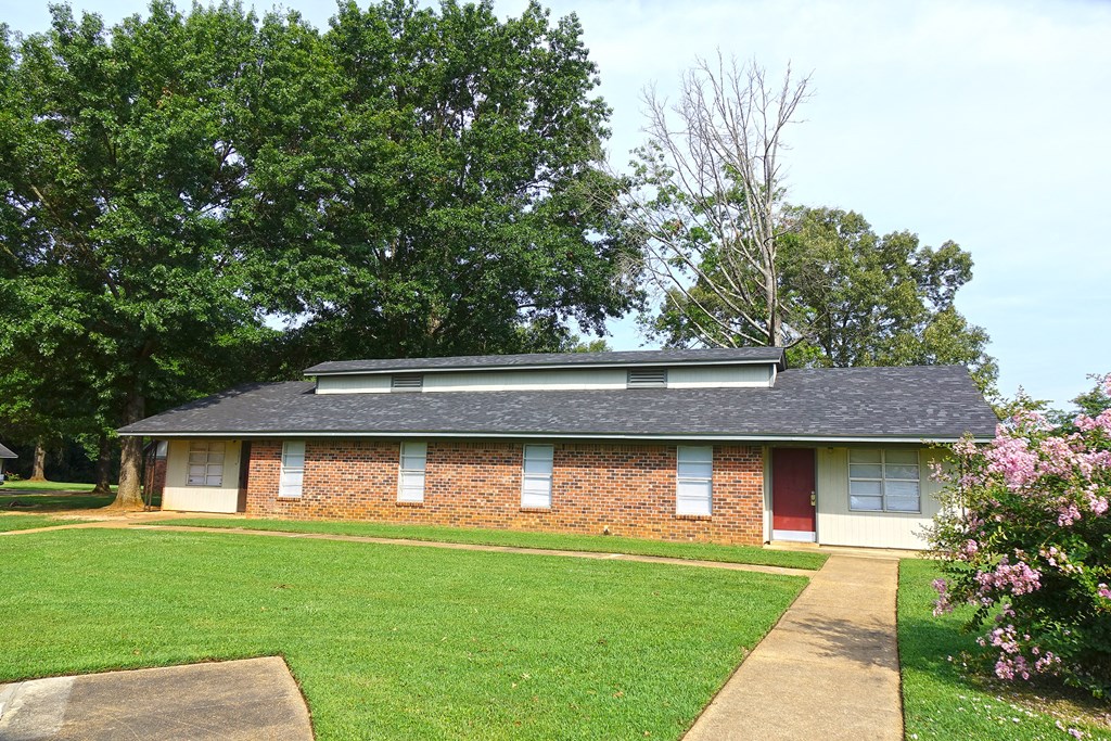the front of a brick house with a lawn and trees
