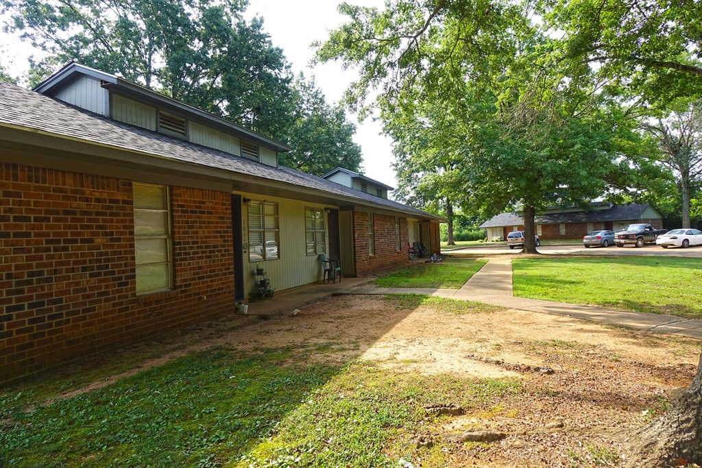 the side of a brick house with a sidewalk and trees