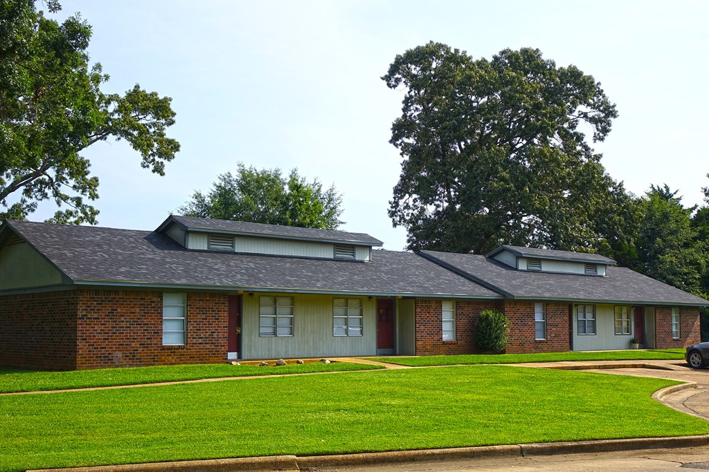 a red brick house with a green lawn and trees