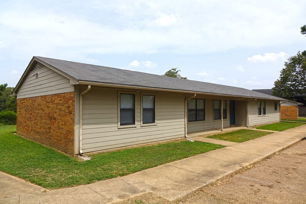 a small tan house with a sidewalk in front of it