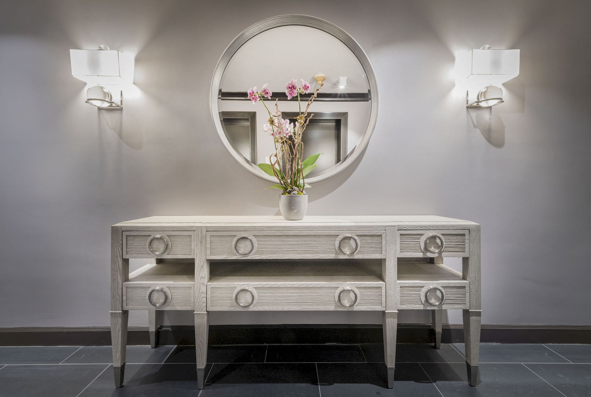 a white console table with a mirror and a vase with flowers