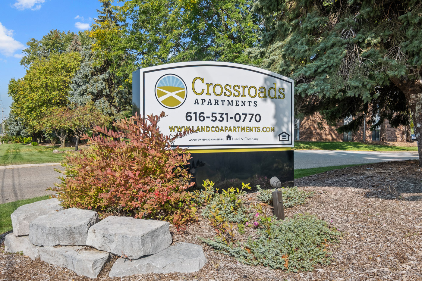 A sign for Crossroads Apartments is displayed in front of some trees.