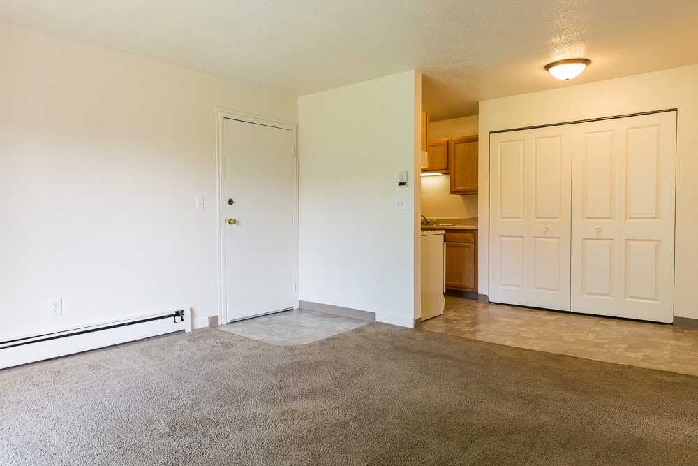 an empty living room with a door to a kitchen