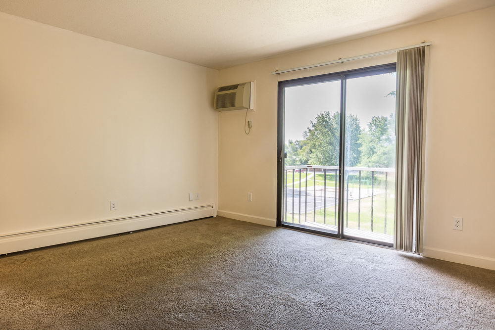 an empty living room with a sliding glass door to a balcony