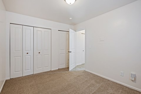A room with white walls and carpeted floor with three white doors.