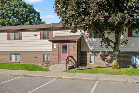 A tree in front of a building with a red door.