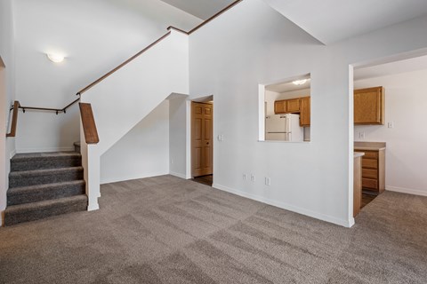 A spacious living room with a staircase and a mirror on the wall.