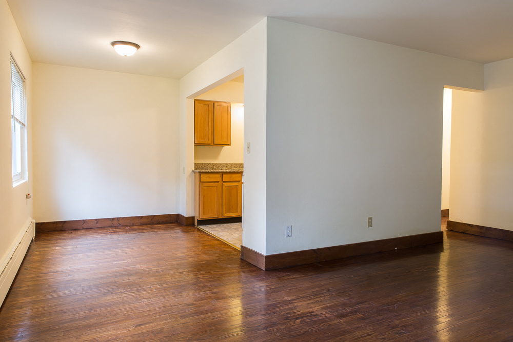 an empty living room with wood floors and a kitchen