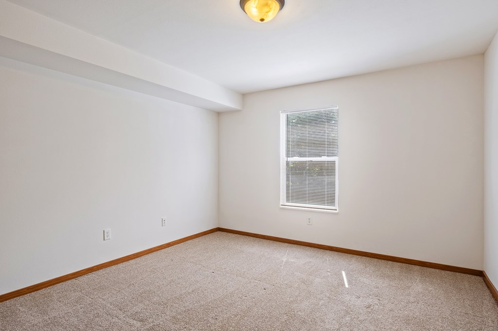 A room with a carpeted floor and a window with blinds.