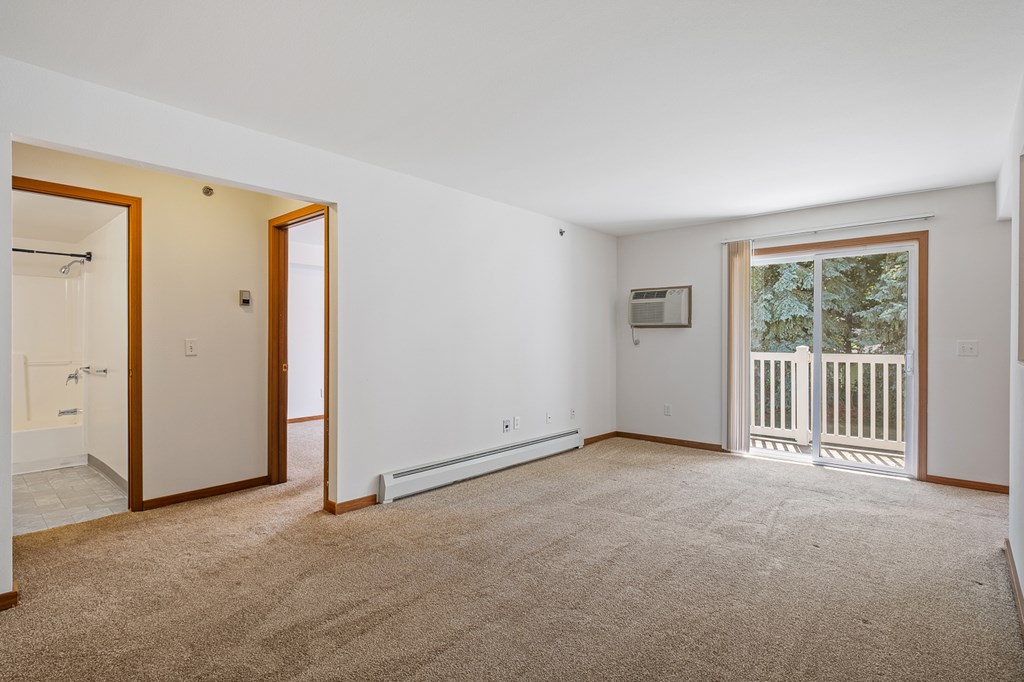 A spacious room with a carpeted floor and a window with a view of a fence and trees.