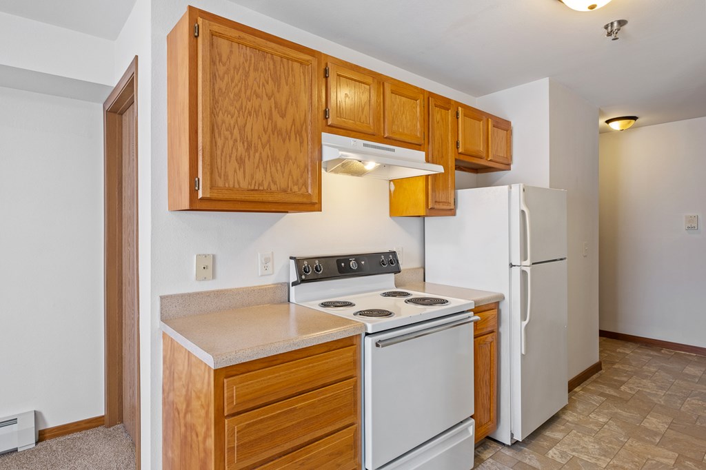 A kitchen with a white refrigerator, white stove, and wooden cabinets.