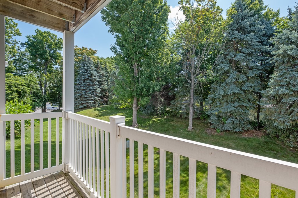 A white wooden porch with a white railing and a view of a green forest.