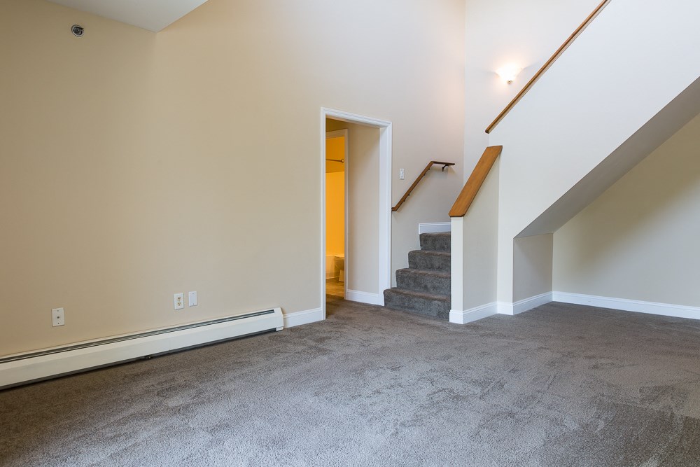 an empty living room with stairs and a carpeted floor