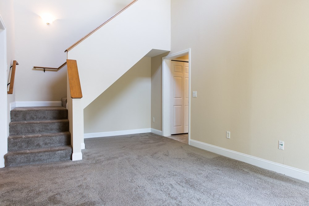 an empty living room with carpeted stairs and a door to a hallway