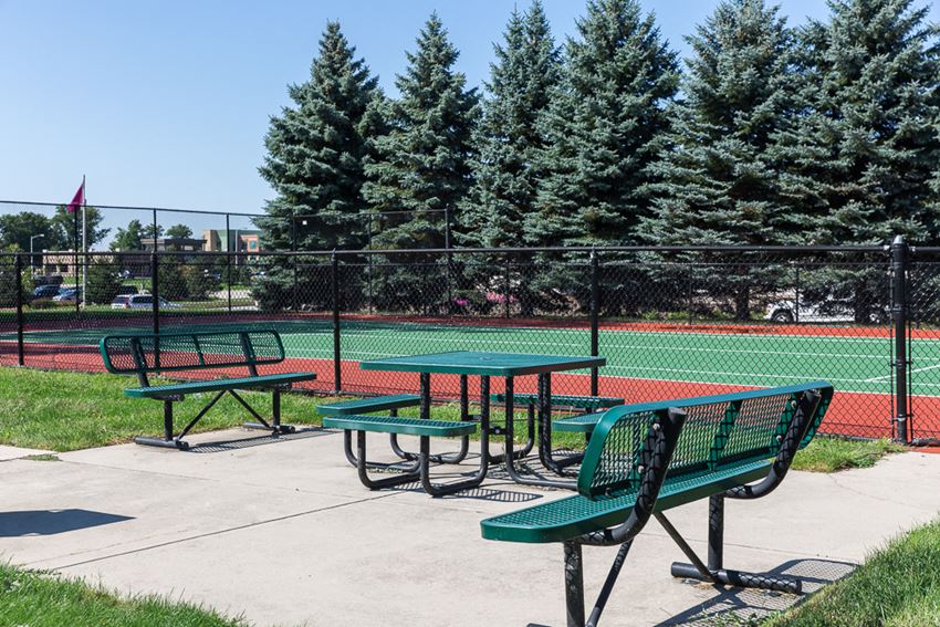 three picnic tables on a sidewalk in front of a tennis court