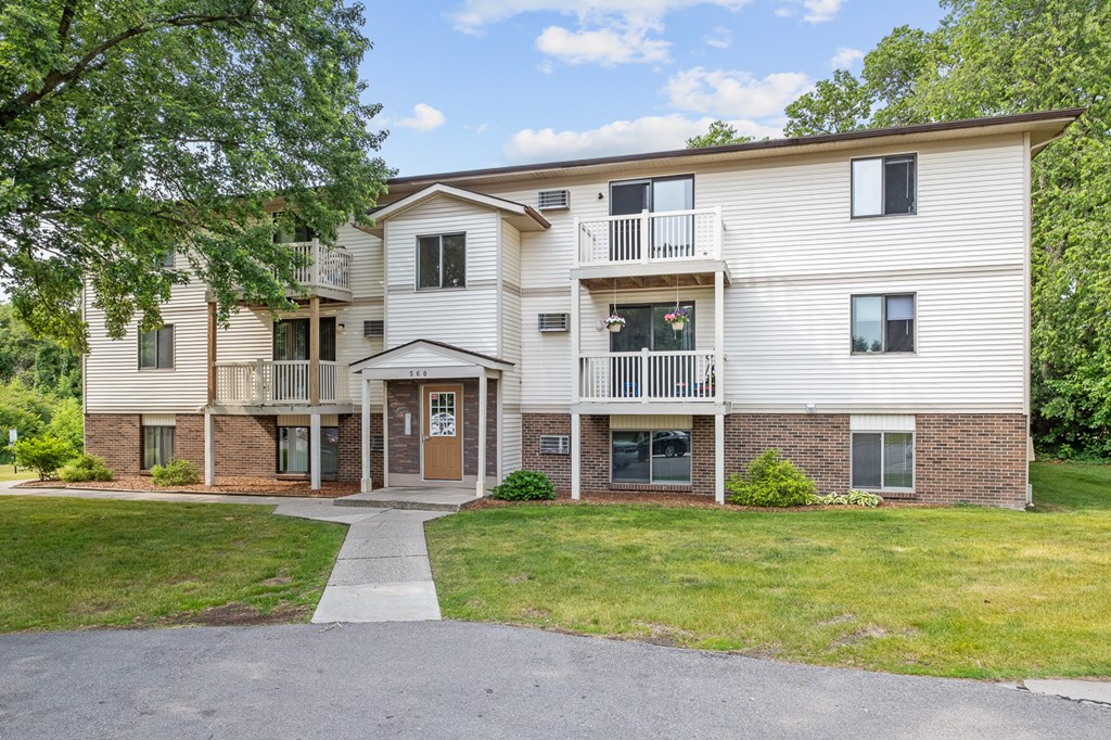 A two-story apartment building with a front lawn and trees.