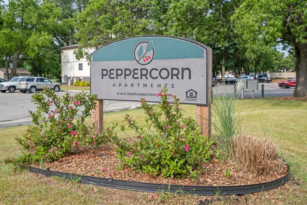 A sign for Peppercorn Apartments is surrounded by flowers and plants.