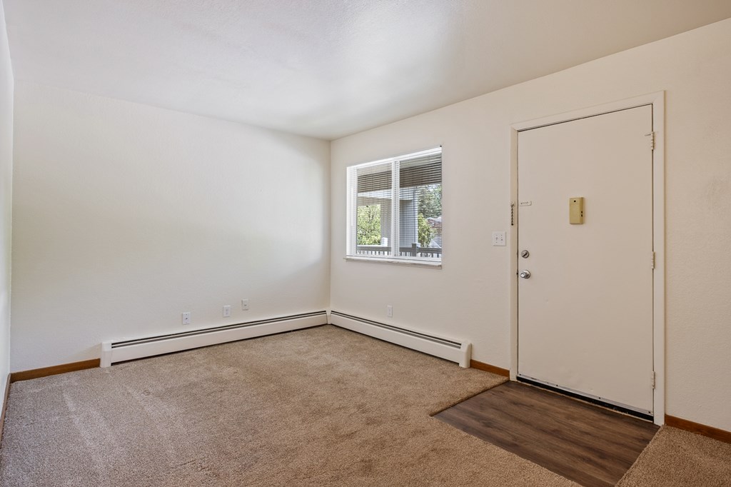 A room with a carpeted floor, a door, and a window with a view of trees.