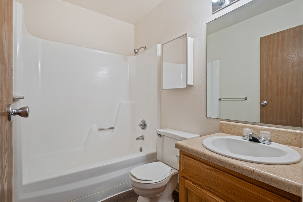 A white bathtub is in a bathroom with a toilet and sink.