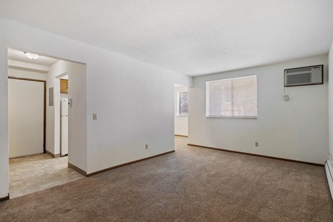 A spacious, empty room with a carpeted floor and a window with blinds.