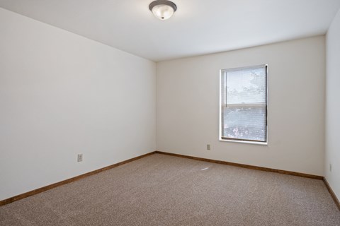 A room with a carpeted floor and a window with blinds.
