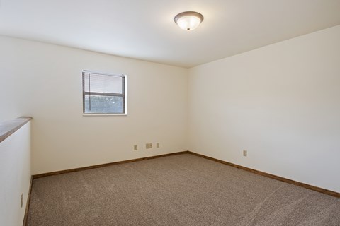 A room with a carpeted floor and a window with blinds.