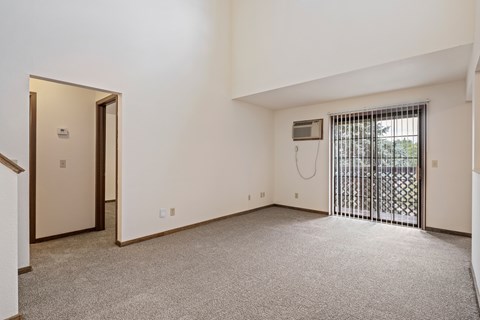 A room with a carpeted floor, a window with a metal grate, and a door with a window.