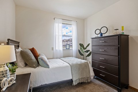 A bedroom with a bed, nightstand, and a plant.