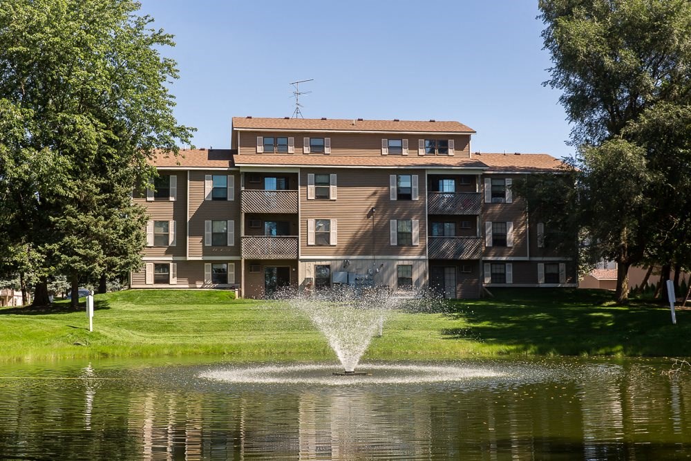 a fountain in the middle of a pond in front of an apartment building