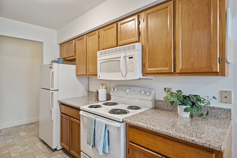 A kitchen with a white refrigerator, white microwave, white stove, and wooden cabinets.