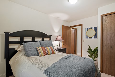 A bedroom with a bed, pillows, a nightstand with a lamp, and a door.