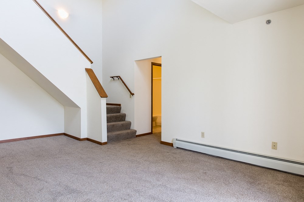 an empty living room with carpet and stairs in a house