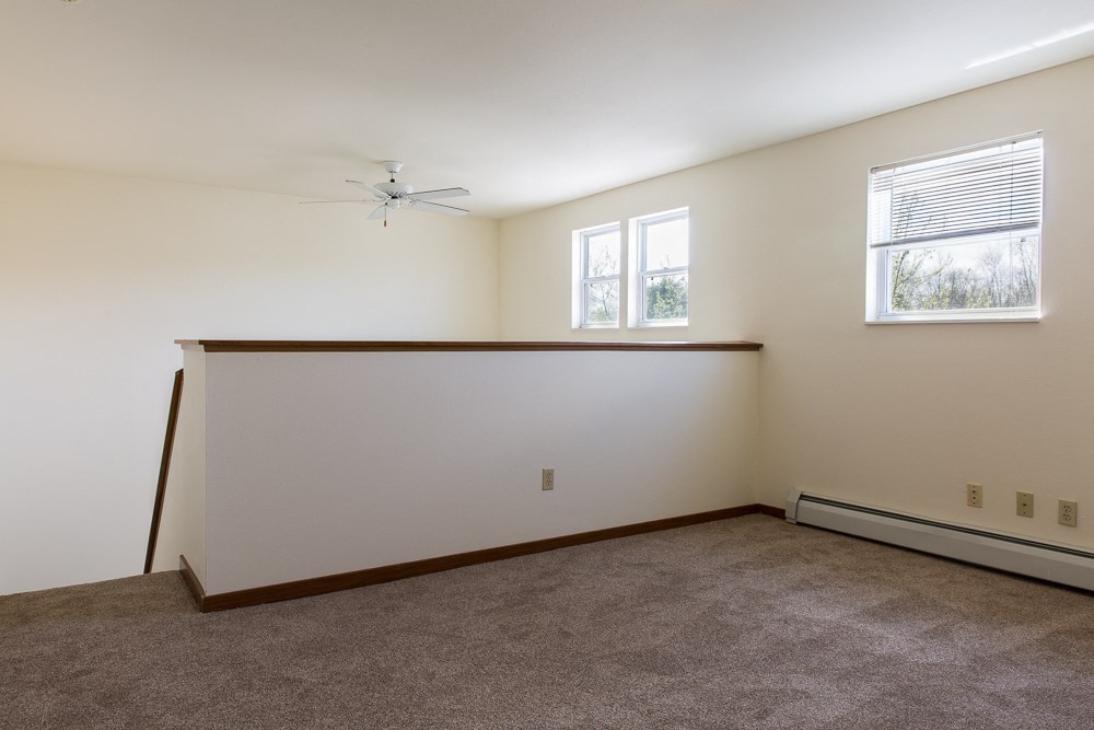 the living room of an empty home with carpet and a ceiling fan