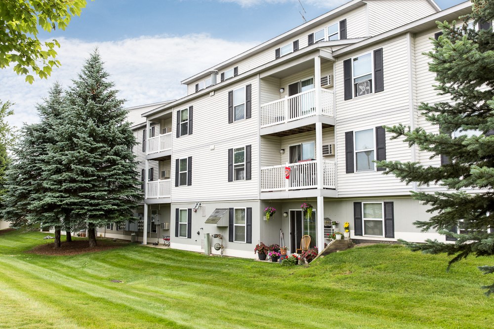 a large white apartment building with a green lawn and trees