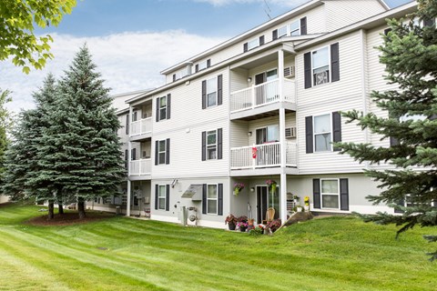 a large white apartment building with a green lawn and trees