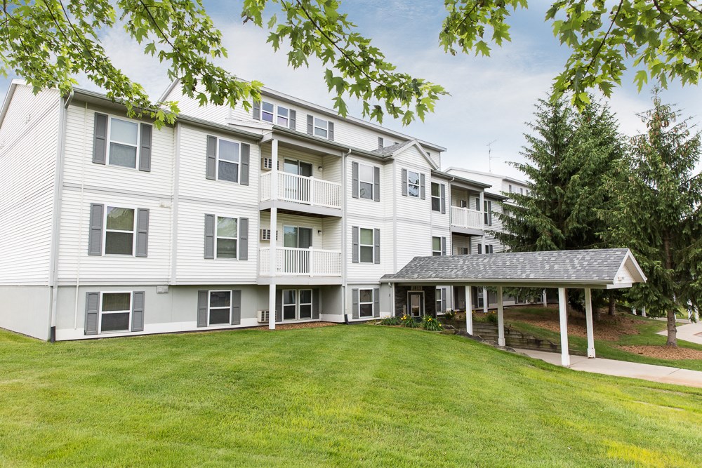 a large white apartment building with a green lawn and trees