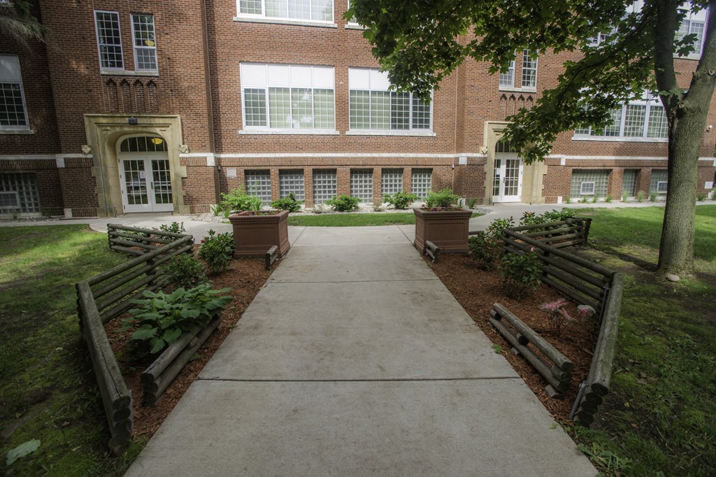 a sidewalk in front of a brick building with trees and benches